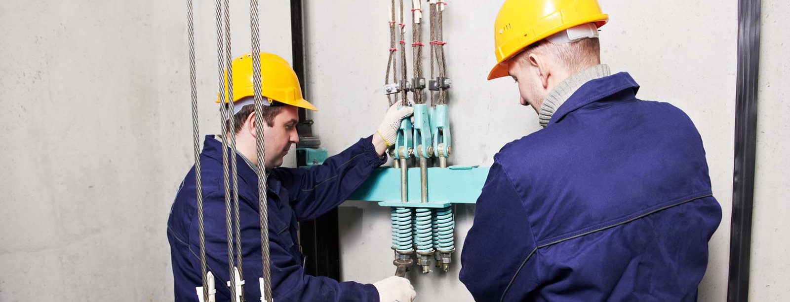 two machinist worker technicians at work adjusting lift with spanners in elevator hoistway